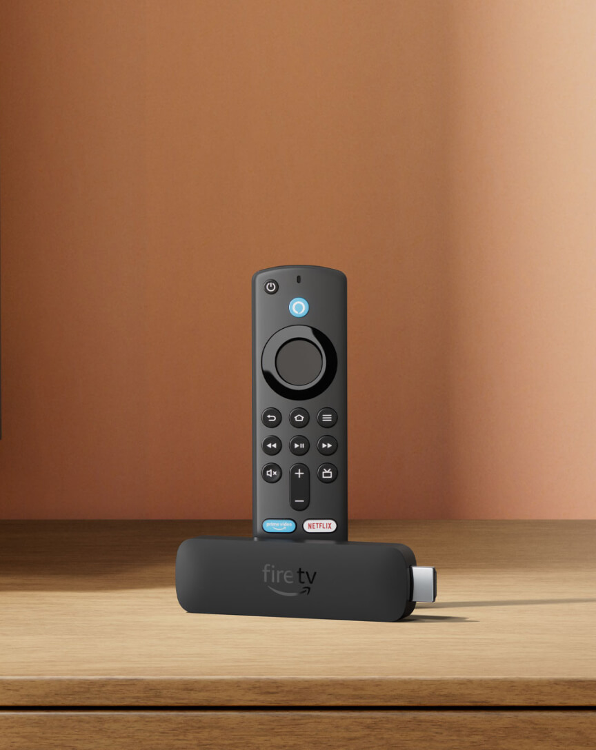 A black TV remote next to a black USB FireStick.