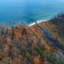 fall woodlands surrounding a riverine path that leads to a large body of water.