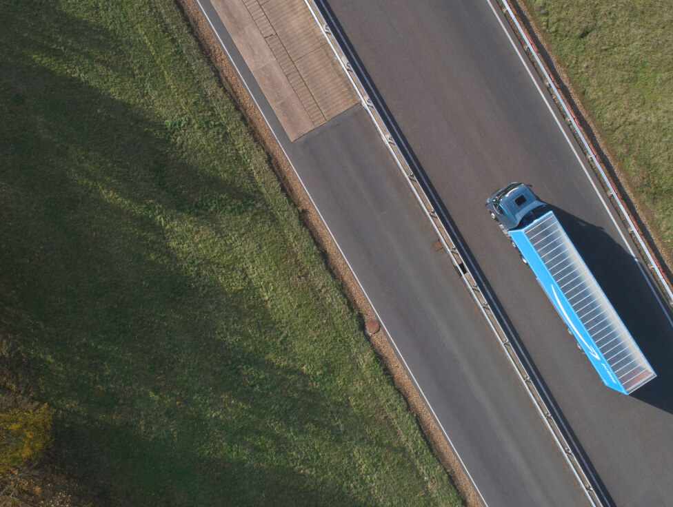 A long-haul Amazon truck is shown from above driving on a road. 