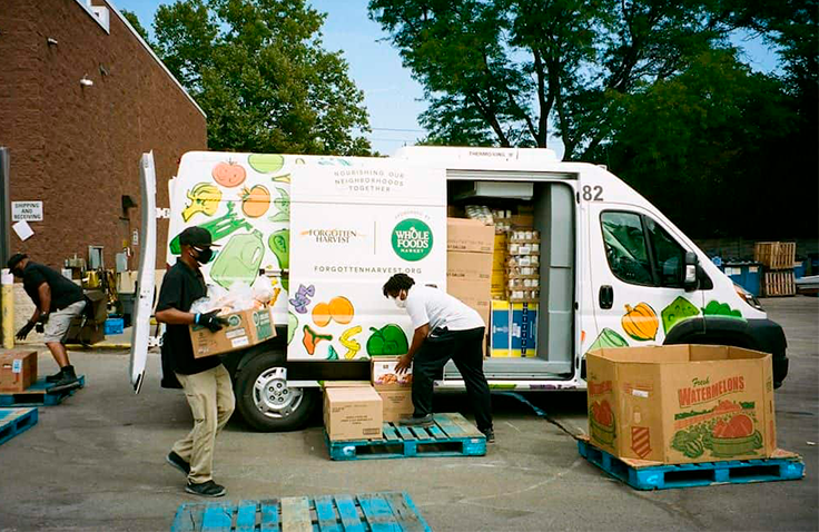 Three people move crates of groceries in front of a Whole Foods branded van.